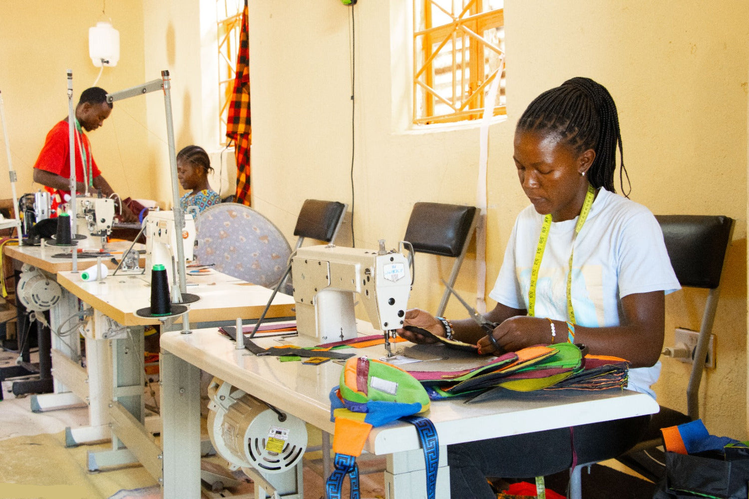 Woman working at a sewing machine in a workshop with other sewing machines and materials.